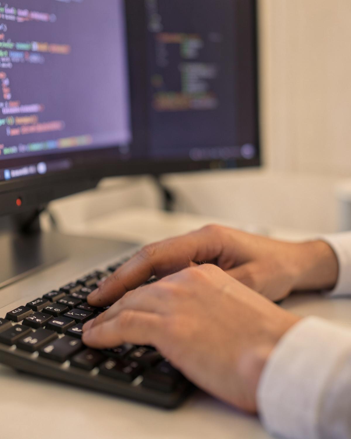 Developer typing at a keyboard in front of a screen of source code